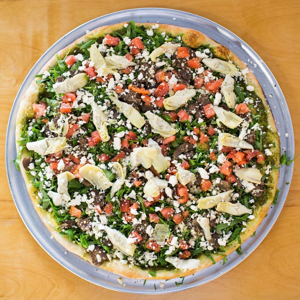 Christian's Pizza with pesto, arugula, diced tomatoes, feta, artichoke hearts, and mushrooms.