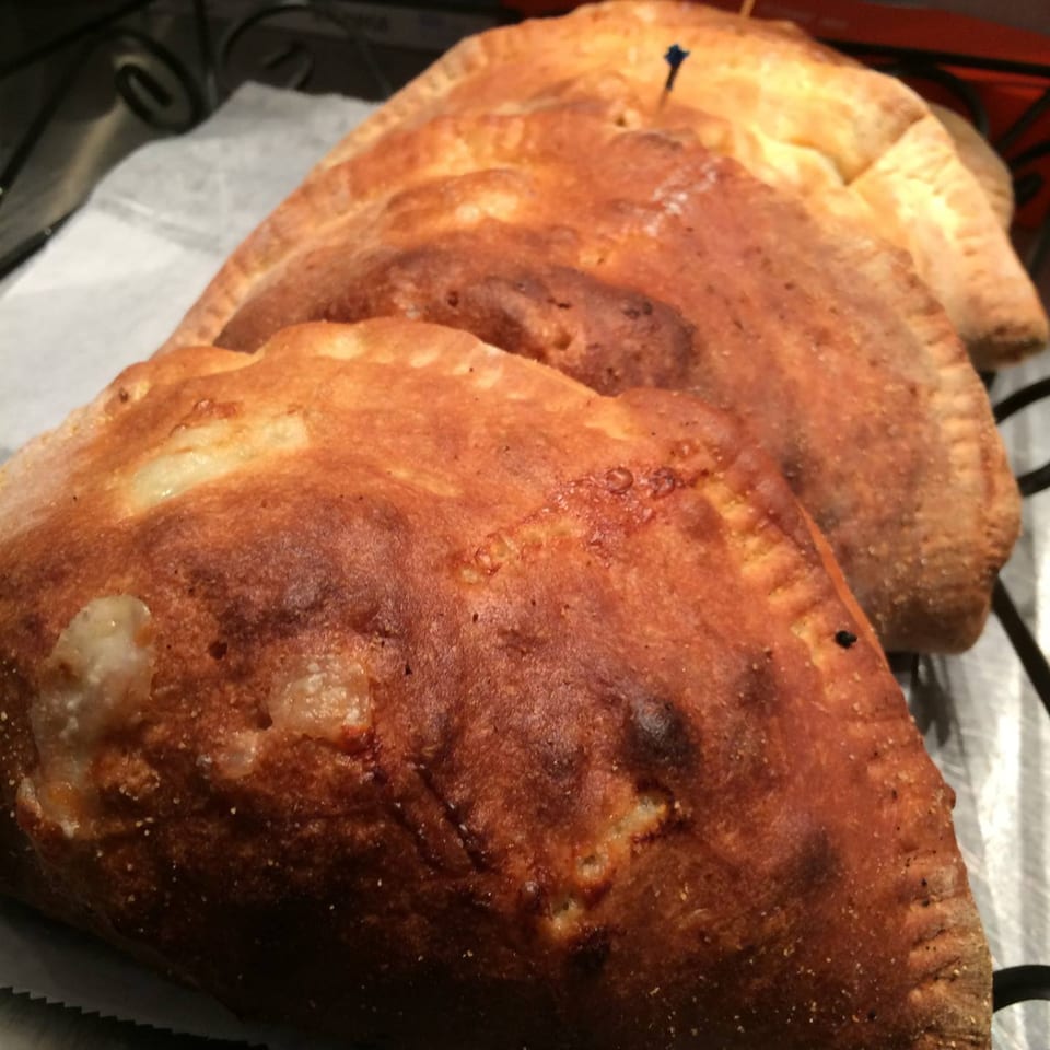 Four golden-brown calzones with crimped edges, one with a toothpick, in a metal basket.